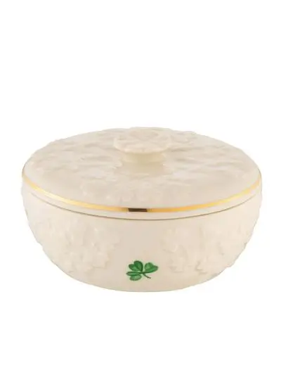 An elegant, round, ivory-colored ceramic dish with a textured surface and a shamrock clover motif, featuring a decorative lid with a floral knob and a gold trim.